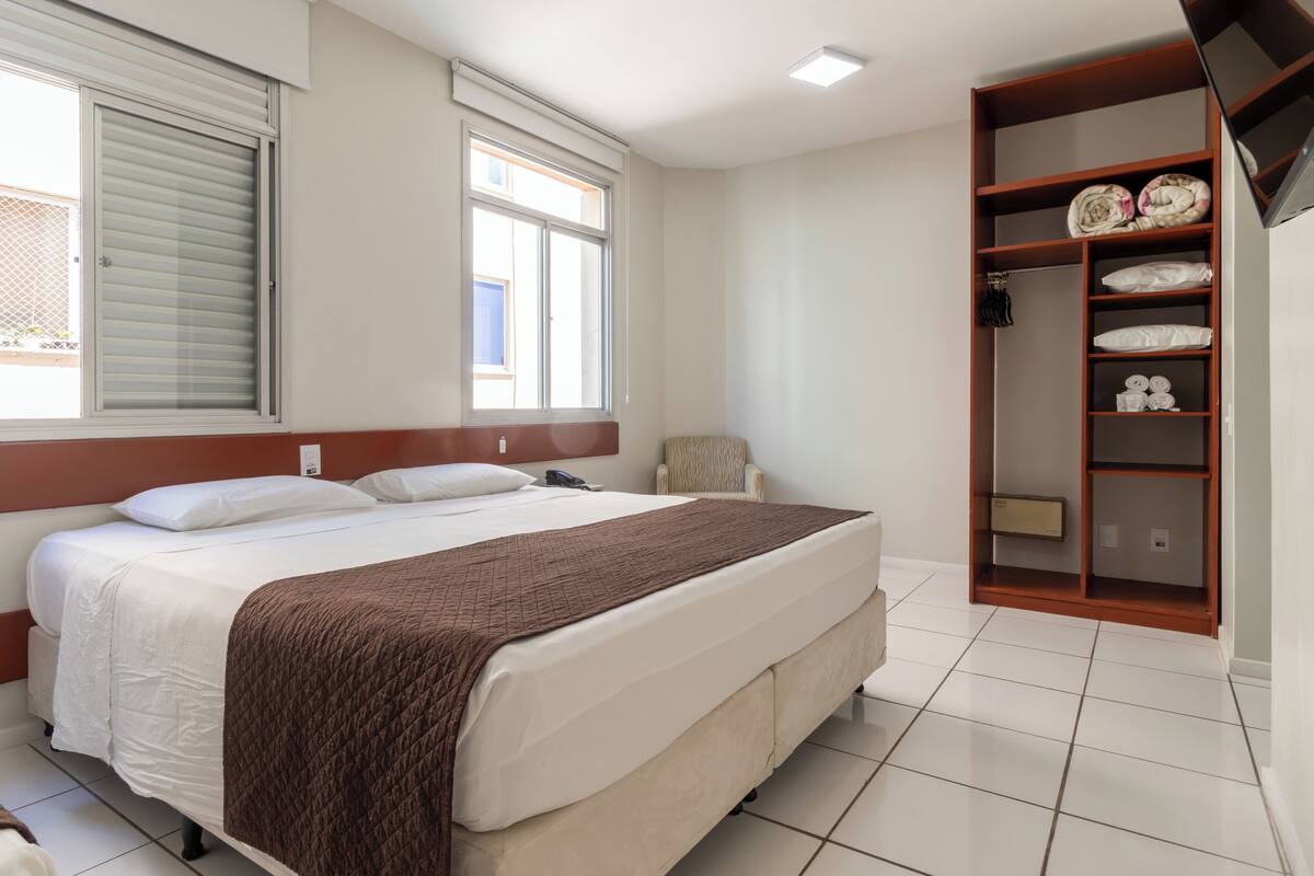 A hotel room with a large bed, a wardrobe, and a window with blinds.