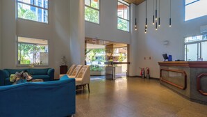 A spacious lobby with a blue sofa, a reception desk, and large windows offering views of the outdoors. - Rio Branco Apart Hotel (Florianópolis)