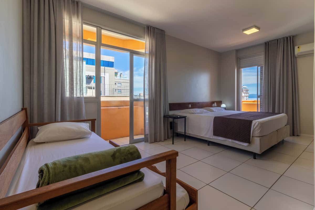 A hotel room with two beds, a balcony, and a view of buildings.