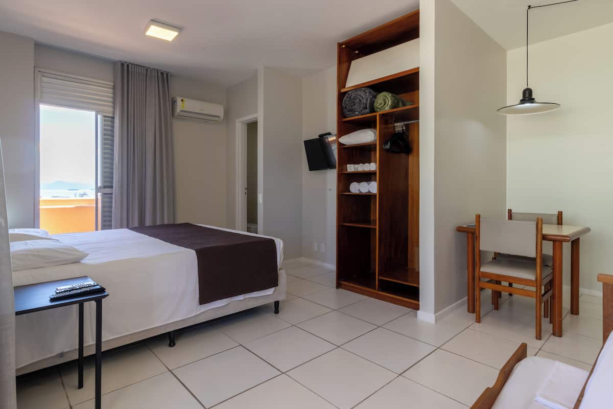 A hotel room with a bed, bedside table, wardrobe, and a small table with a chair.