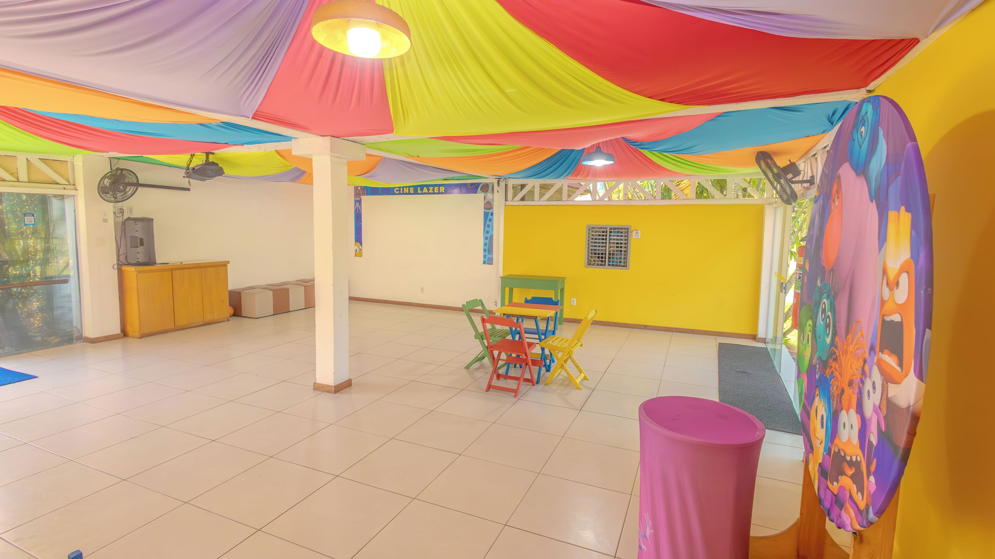 A spacious room with a tiled floor, colorful draped ceiling, and a yellow wall.