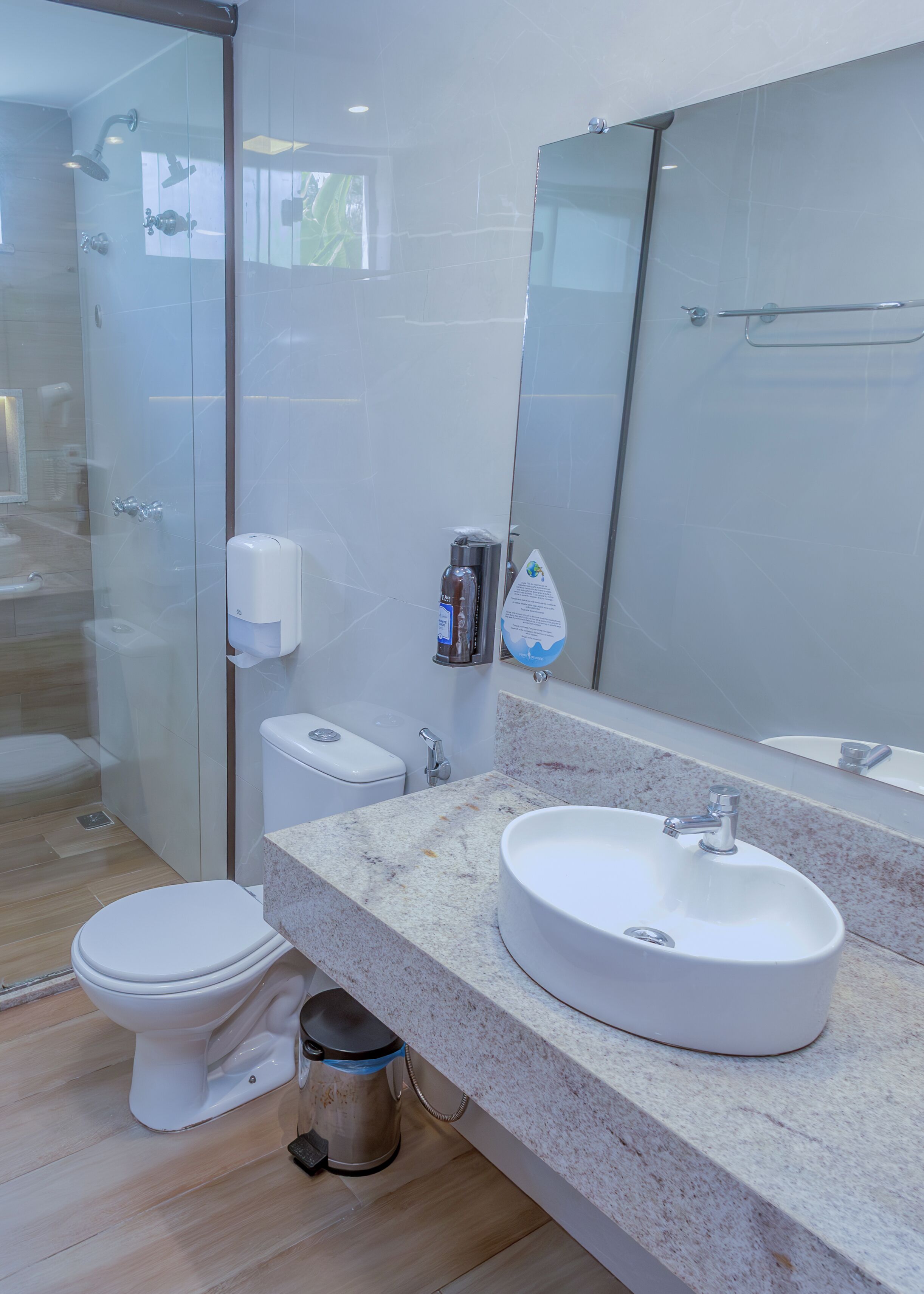 A modern bathroom with a glass shower enclosure, a toilet, a sink with a marble countertop, and a large mirror.