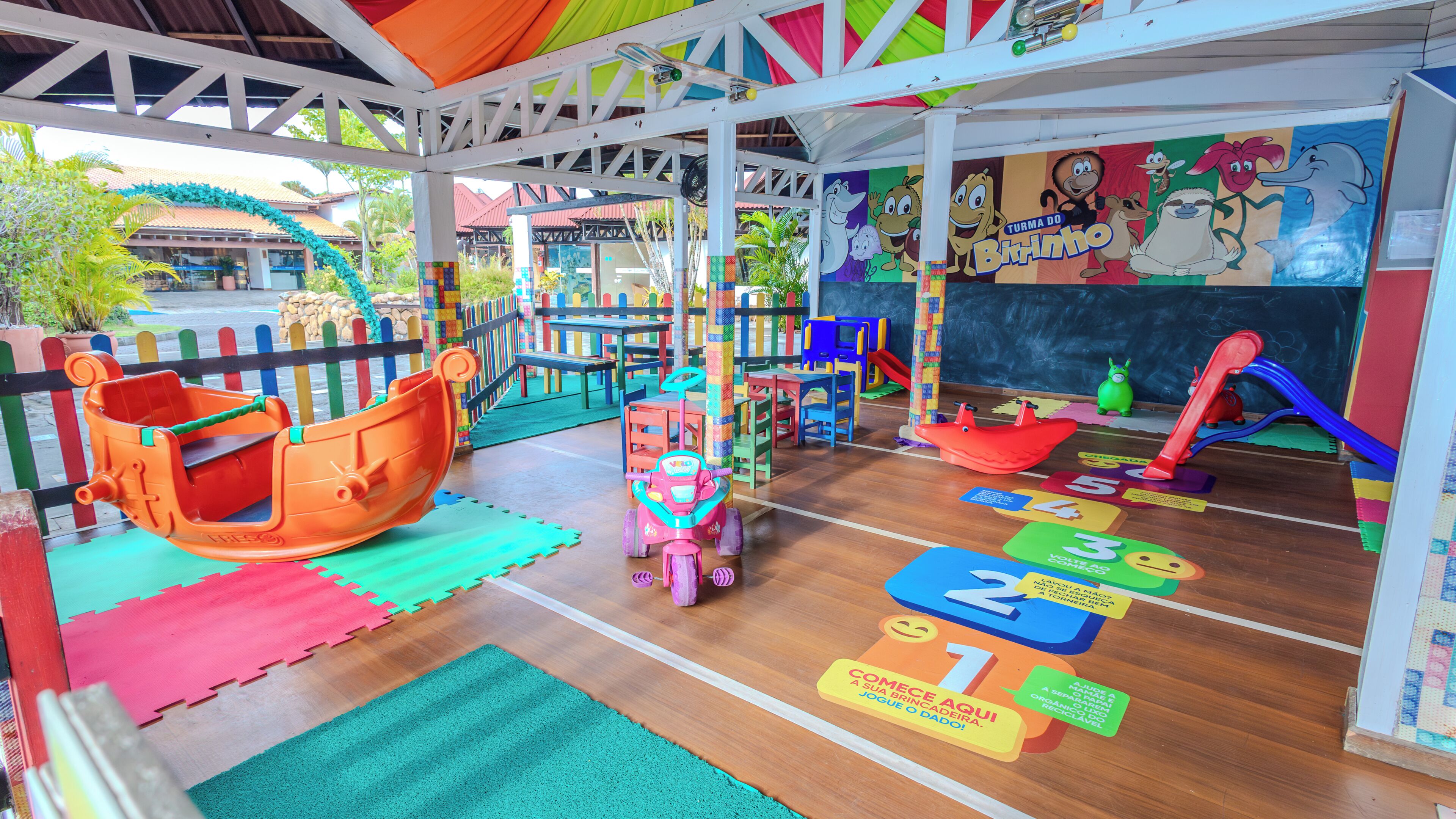 Un área de juegos infantiles con estructuras coloridas, alfombras educativas y un mural.