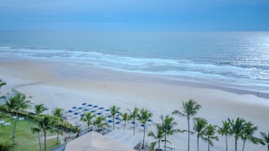 A beach resort with a sandy beach, palm trees, and umbrellas.