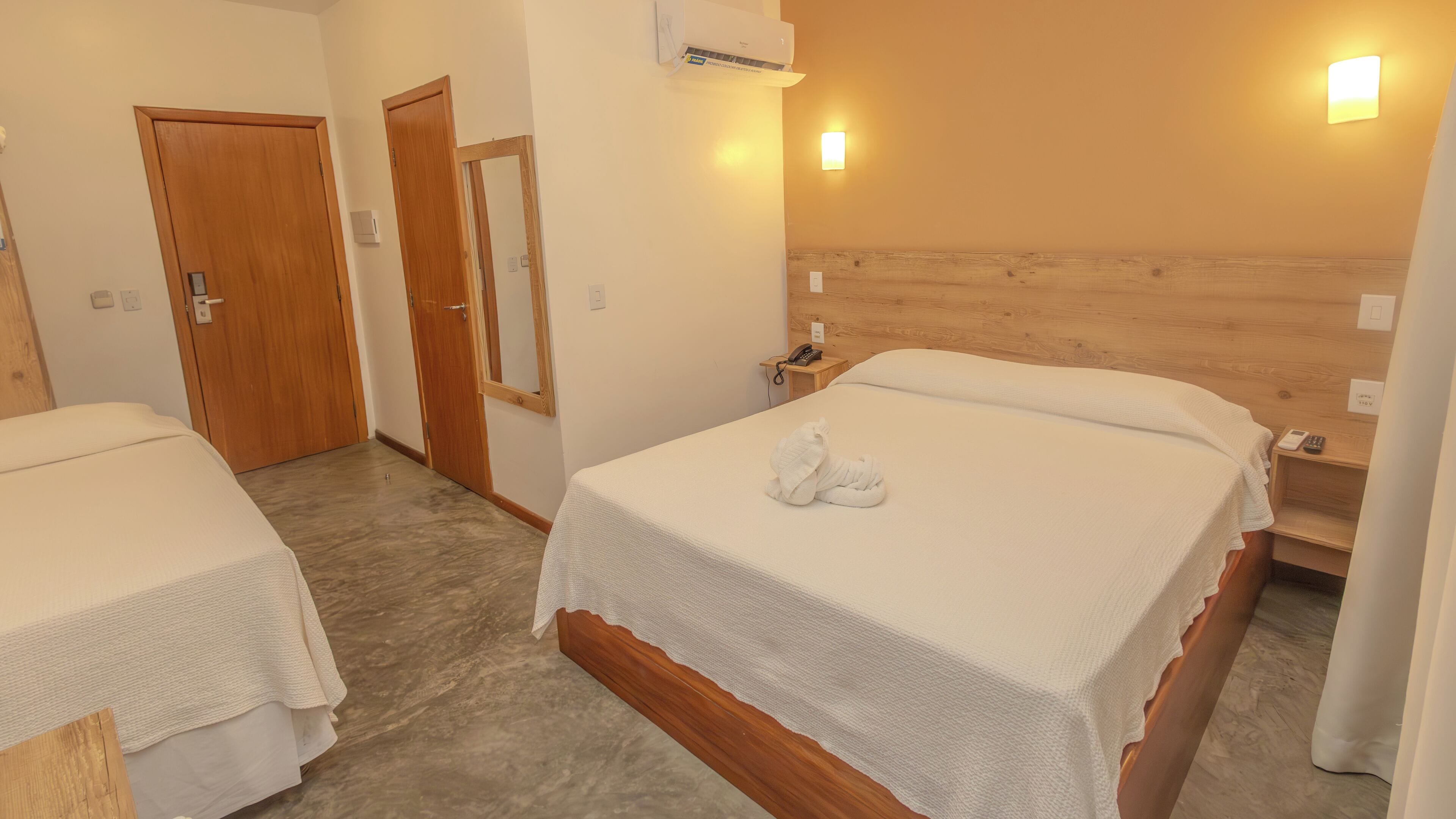 Habitación de hotel con dos camas, cabeceros de madera, una mesita de noche con teléfono y aire acondicionado instalado en la pared.
