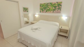 A hotel room with a bed, a bedside table, a nightstand, a mirror, and a wall-mounted painting.