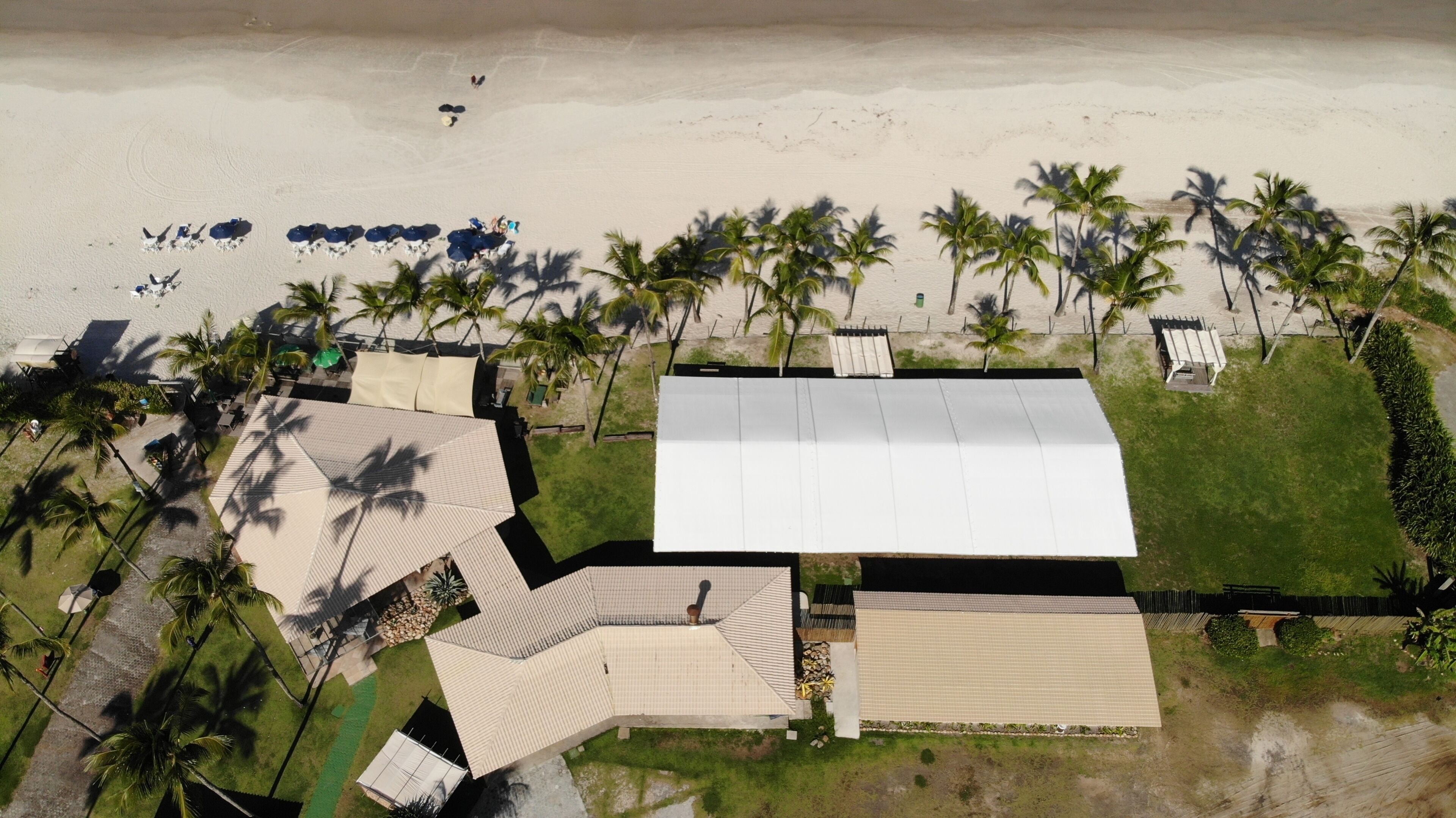 An aerial view of a resort with multiple buildings, a beach, and palm trees.
