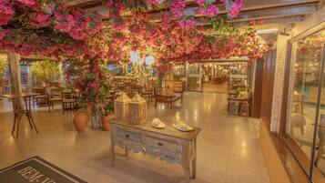 Un vestíbulo amplio con una zona decorativa central que presenta un gran macetero, una mesa de estilo vintage con zapatos y flores rosas colgantes.