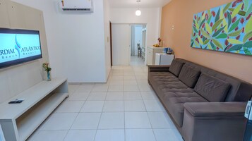 Uma sala de estar moderna com televisão de tela plana, um sofá, uma mesa de centro e ar condicionado fixado na parede.