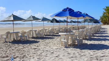 Na praia, areia branca, espreguiçadeiras, guarda-sóis 