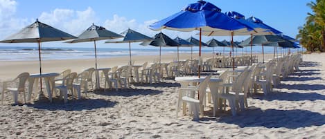 Na praia, areia branca, espreguiçadeiras, guarda-sóis 