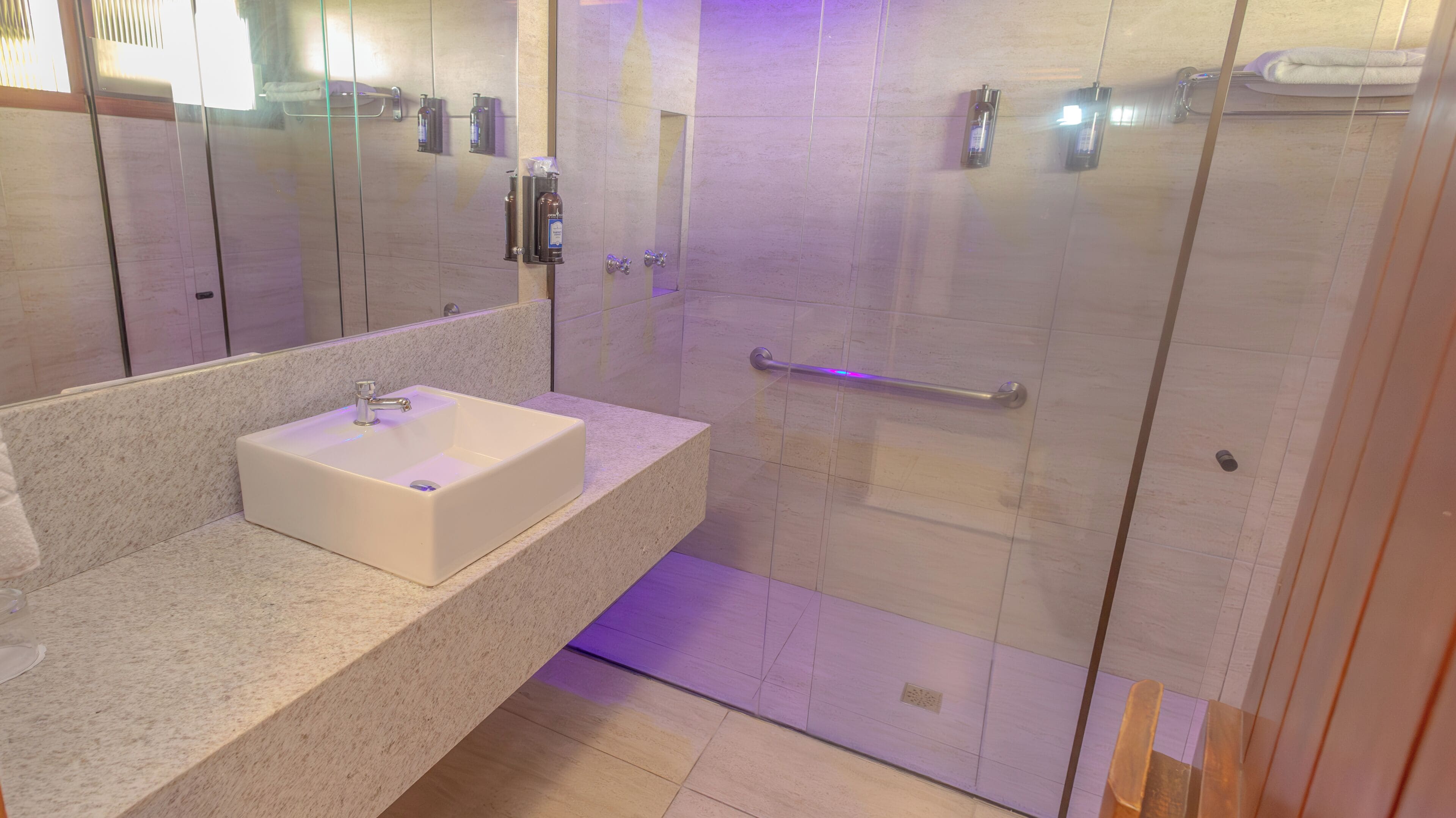 Un baño moderno con un lavamanos blanco, cabina de ducha con mampara de vidrio y barra de apoyo.