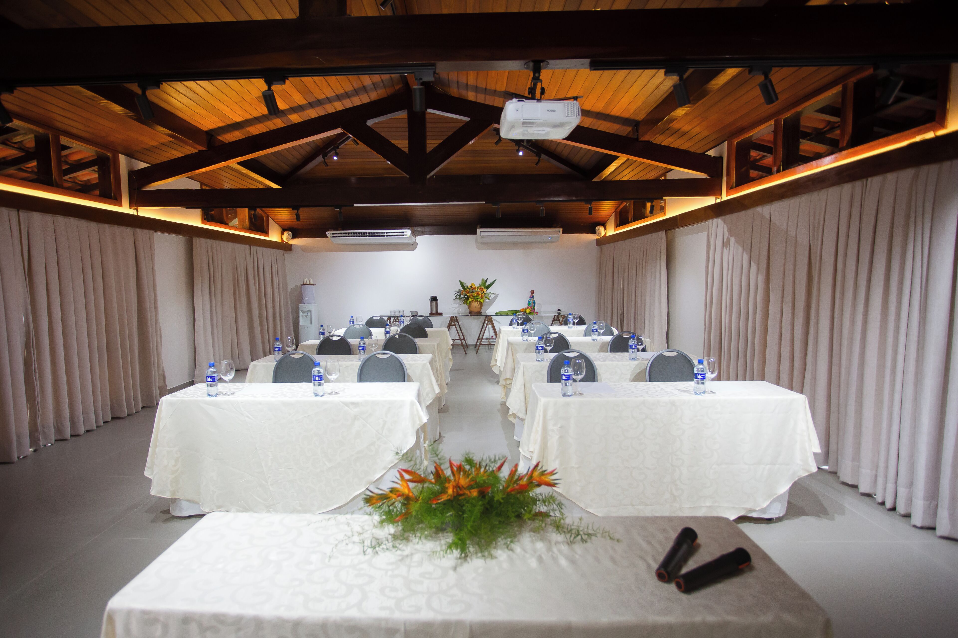 A conference room with tables set up for a meeting, featuring a projector and an air conditioning unit.