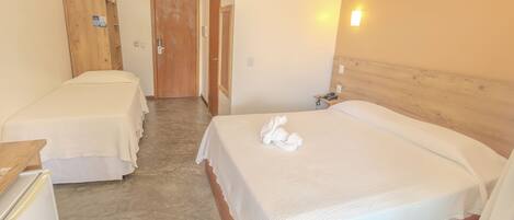A hotel room with two single beds, a wooden wardrobe, a small desk with a telephone, and a wall-mounted air conditioner.