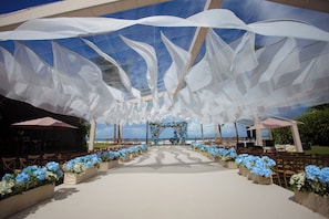 An outdoor wedding venue with a white aisle, floral arrangements, and a view of the ocean.