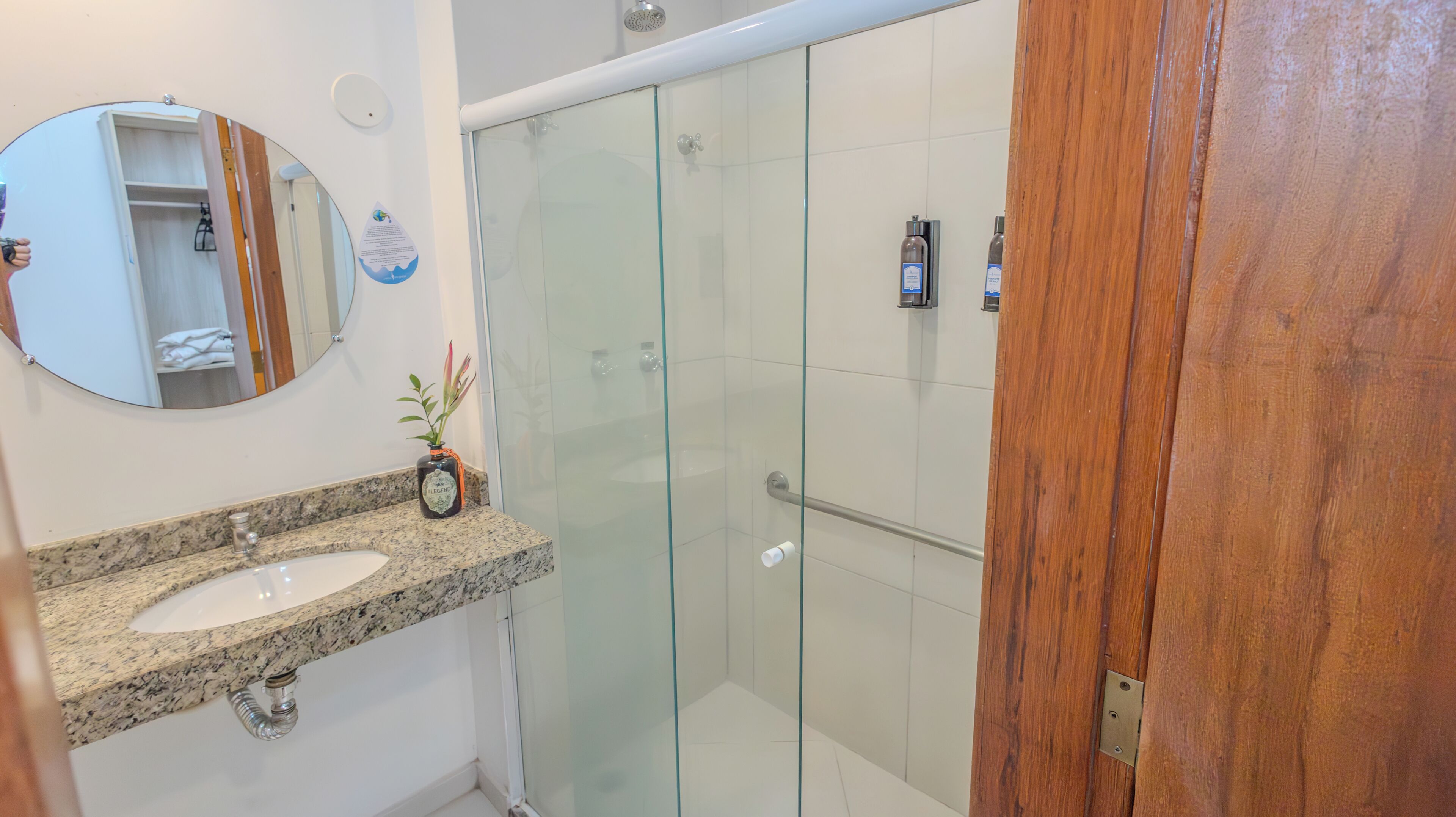 A bathroom with a granite countertop sink, a glass shower enclosure, and a wooden door.