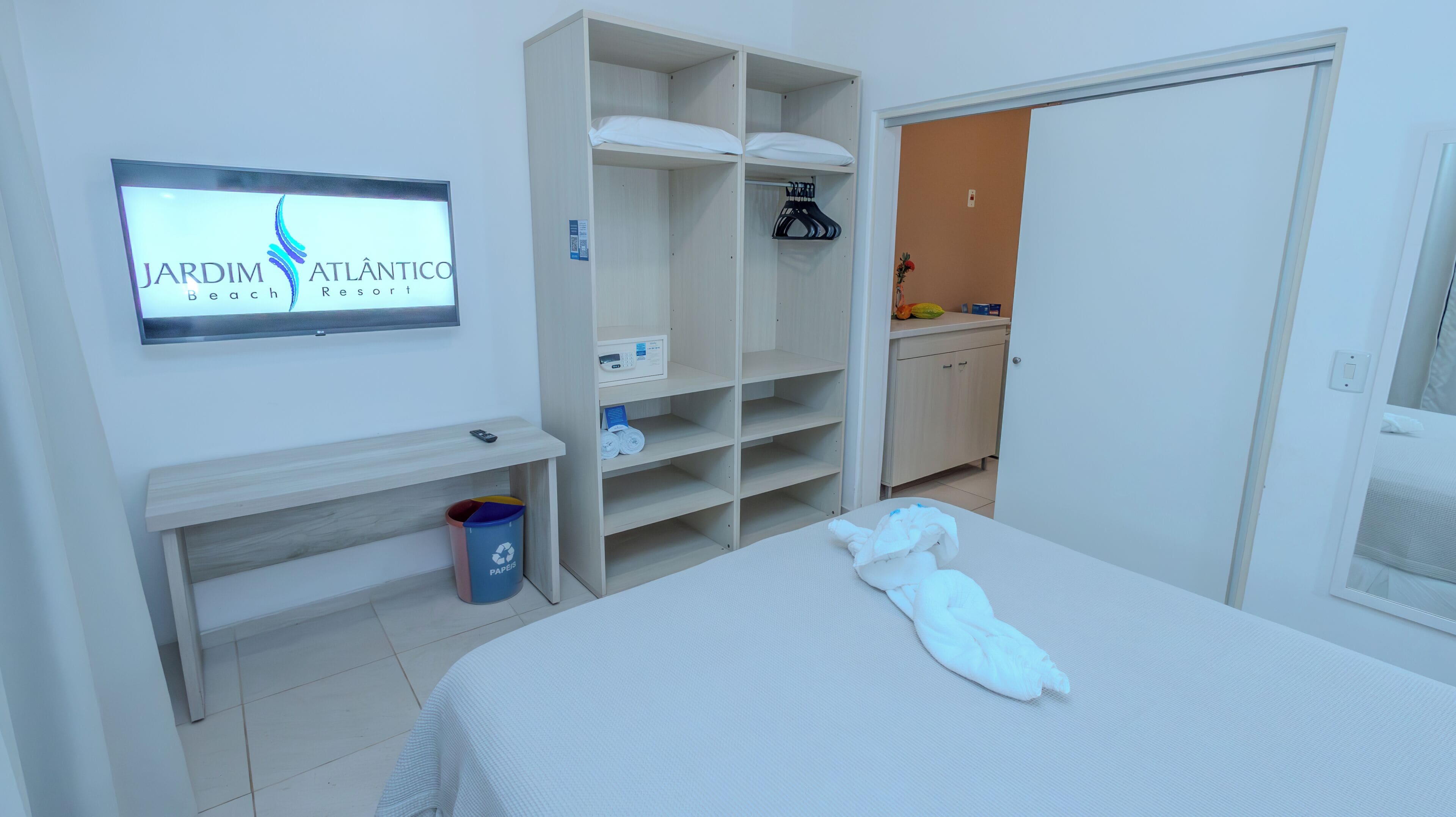 Una habitaci ón de hotel con una cama, un armario, una mesita, un cubo de basura y un cartel en la pared.