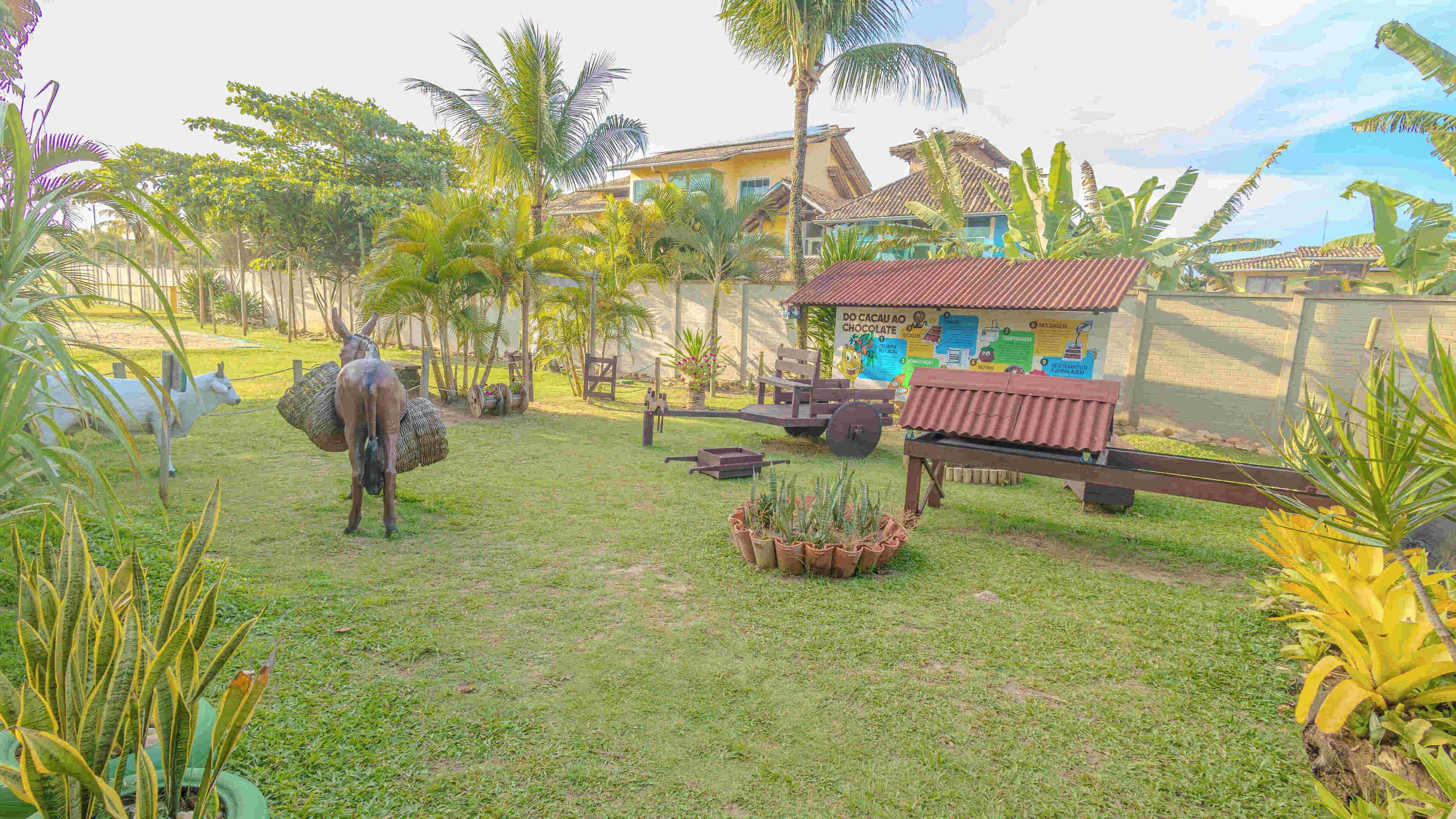 A grassy area with a wooden bench, a donkey sculpture, and a small structure with a sign.