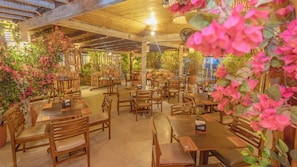 Un restaurante con mesas y sillas de madera, plantas en macetas y techo de madera.
