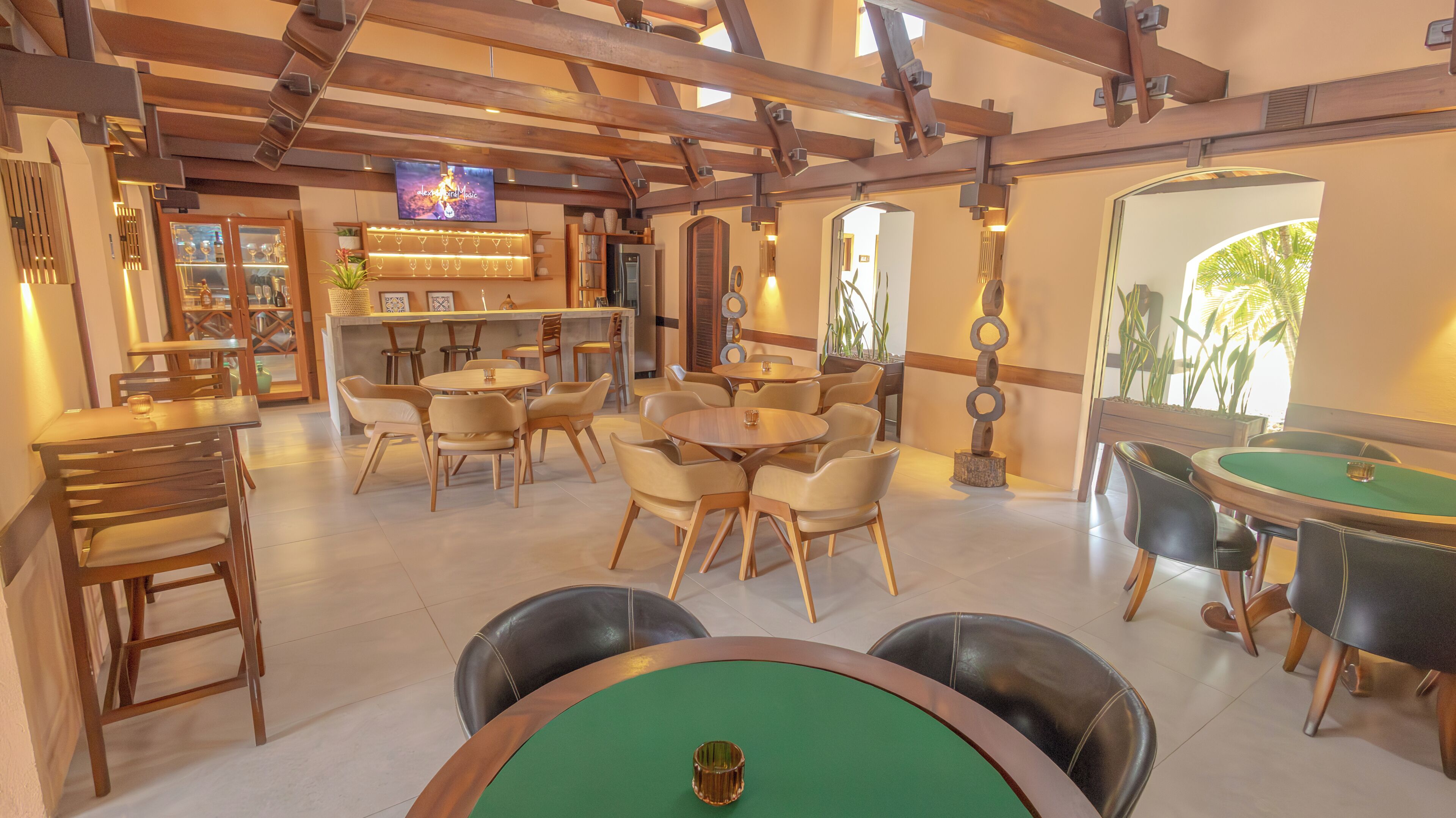 A spacious indoor area with multiple seating arrangements, a billiards table, and a television screen displaying a program.