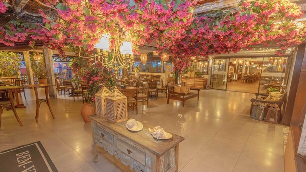 Un vestíbulo amplio con mobiliario de madera, un árbol decorativo en el centro y suelo de baldosas.