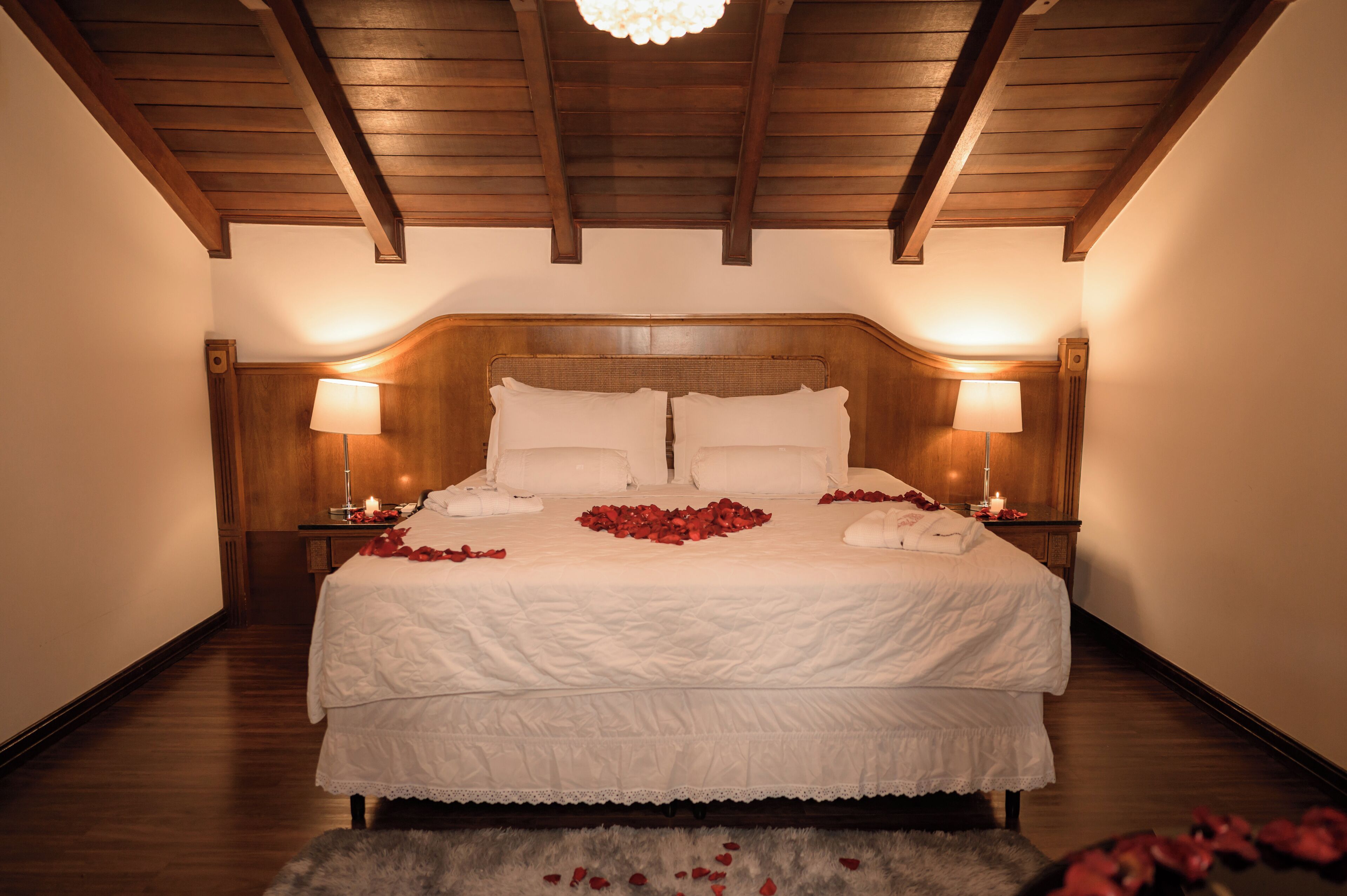 Una cama grande con sábanas blancas, dos lámparas de noche y pétalos de rosa sobre la cama.