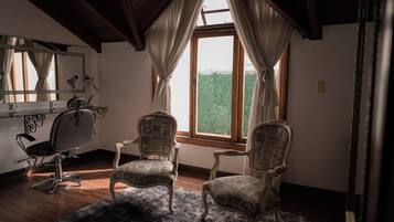 Une pièce comprenant deux fauteuils rembourrés, un bureau avec une chaise, un miroir et une fenêtre avec des rideaux.