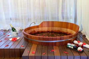 A wooden bathtub filled with water and rose petals, surrounded by a wooden bench. - Terra Boa Hotel Boutique (Itacaré)