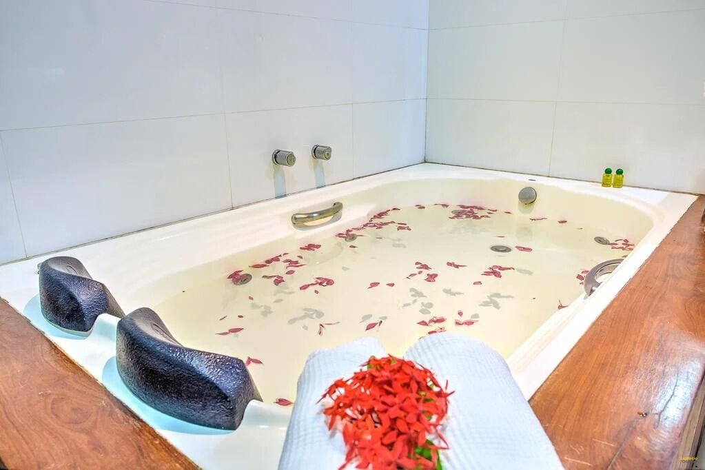 A bathtub with rose petals, a towel, and two bottles of bath products.