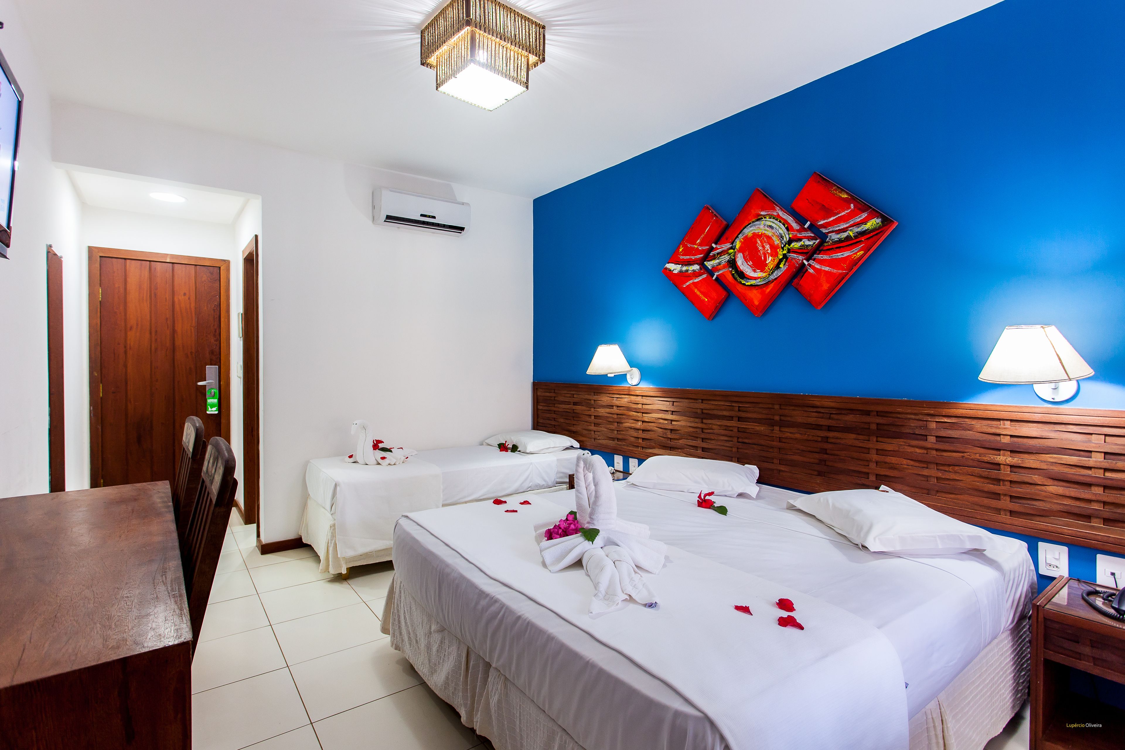 Quarto de hotel com duas camas, cabeceira de madeira, parede azul e escrivaninha de madeira.