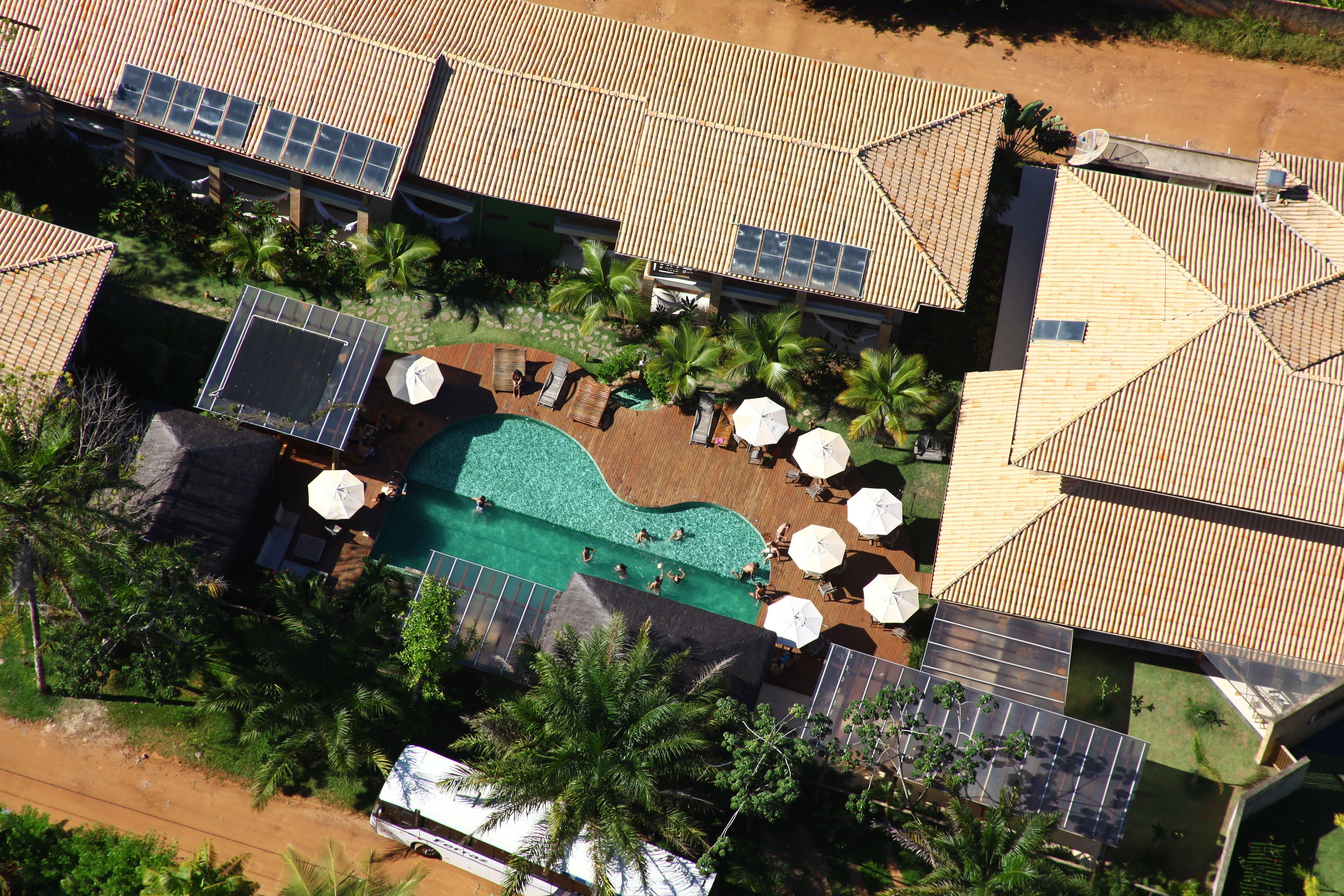 An aerial view of a resort with a swimming pool, sun loungers, and solar panels.