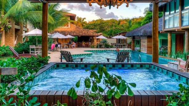 A pool area with lounge chairs, umbrellas, and a thatched-roof building. - Terra Boa Hotel Boutique (Itacaré)