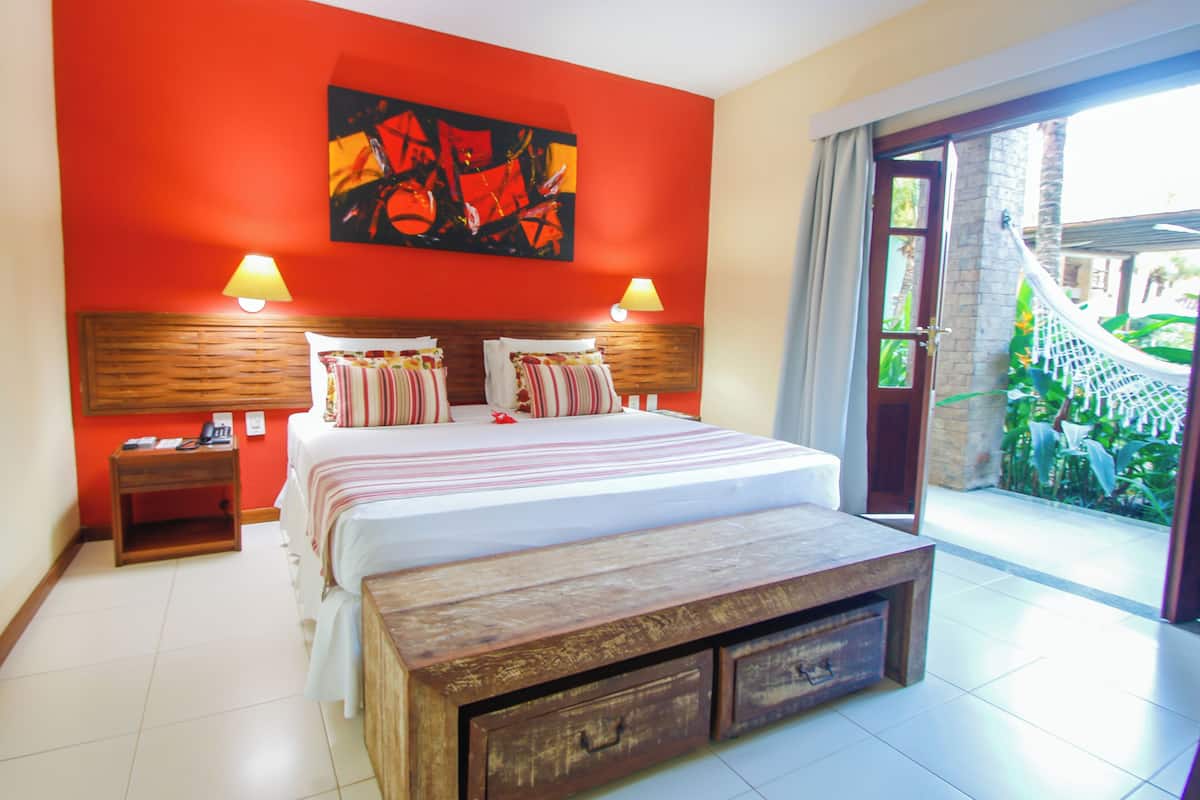 Una camera da letto con un letto grande, due abat-jour, una panca in legno e vista su un giardino attraverso una porta aperta.