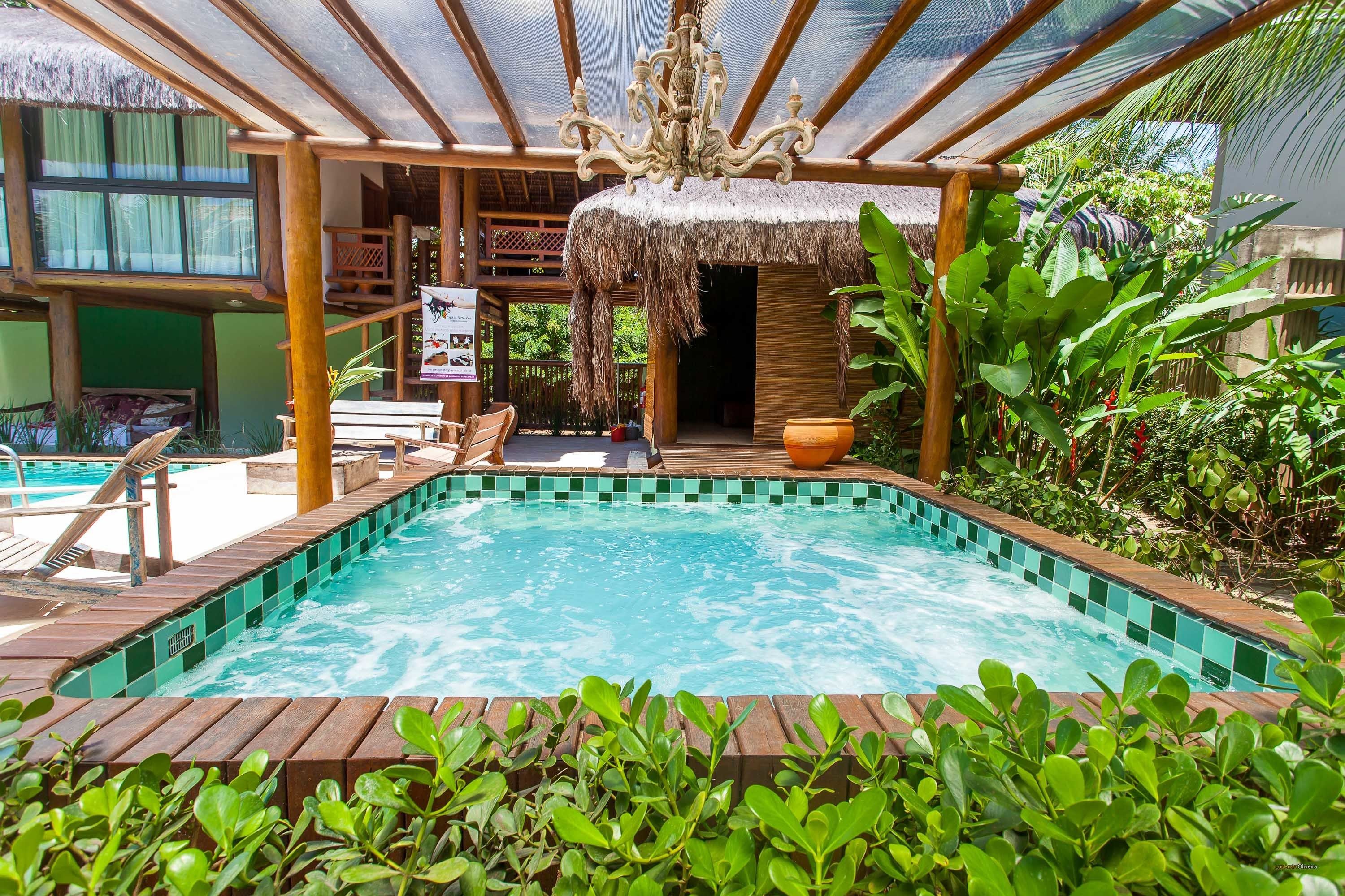 Un área de piscina con terraza de madera, sillas de descanso y una estructura de techo de paja.