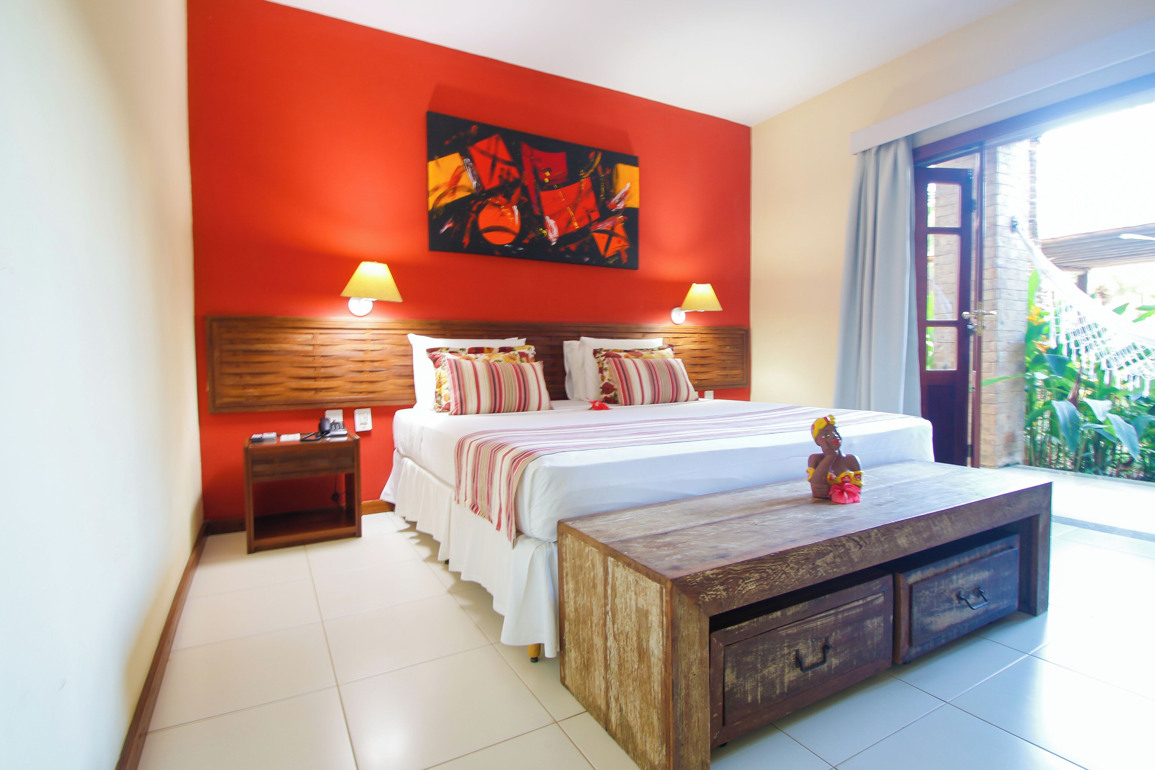 Un dormitorio con cama, mesitas de noche, un banco de madera y un ventanal grande.