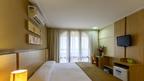 A hotel room with a bed, a desk, a television, and a window with curtains. - Rede Andrade Bello Mare Comfort (Natal)