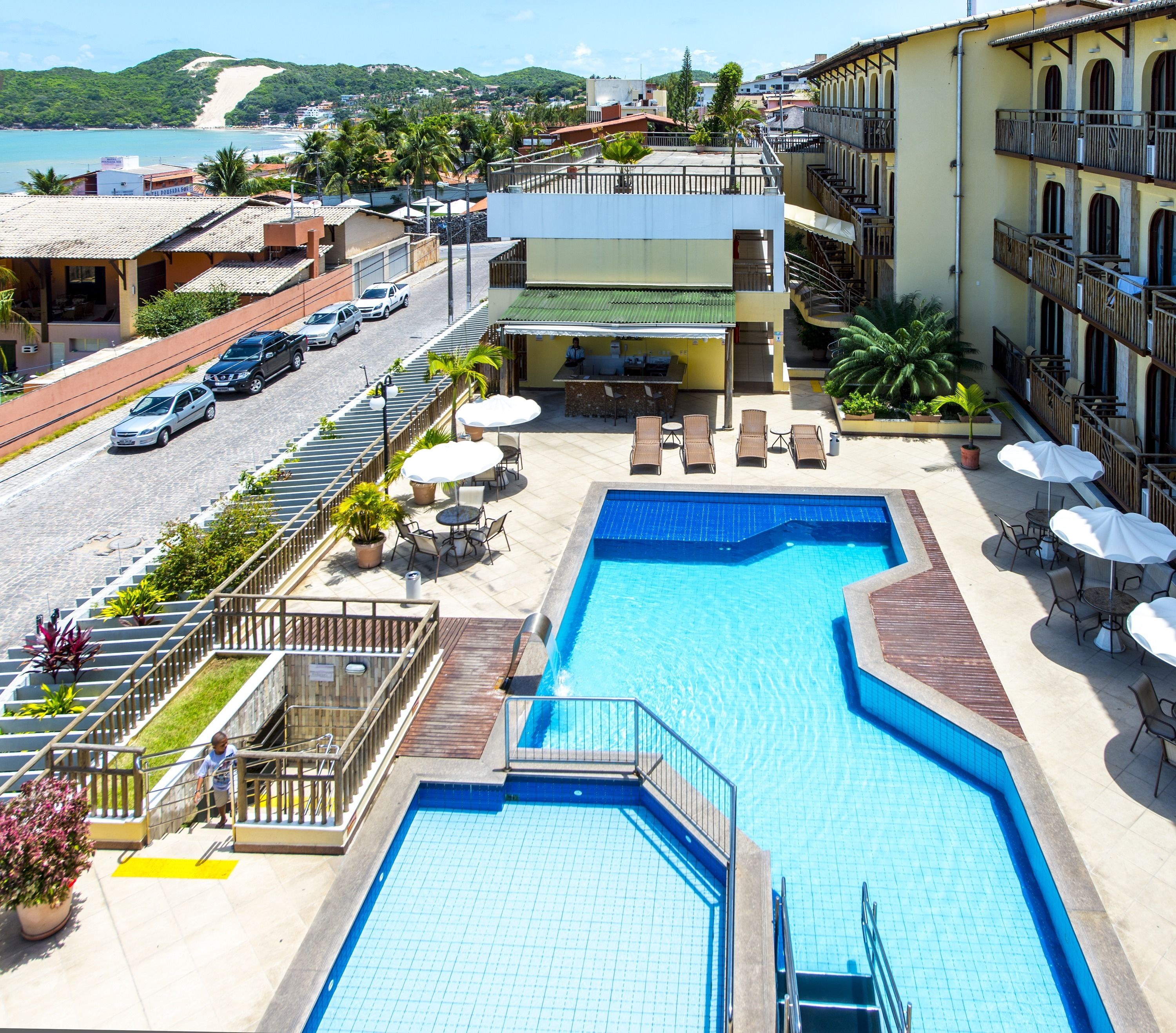 A hotel with a swimming pool, outdoor seating, and a view of the beach.