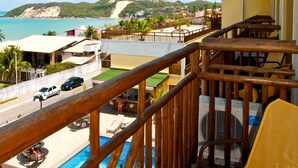 A balcony with wooden railings overlooking a swimming pool and a view of the beach and ocean. - Rede Andrade Bello Mare Comfort (Natal)