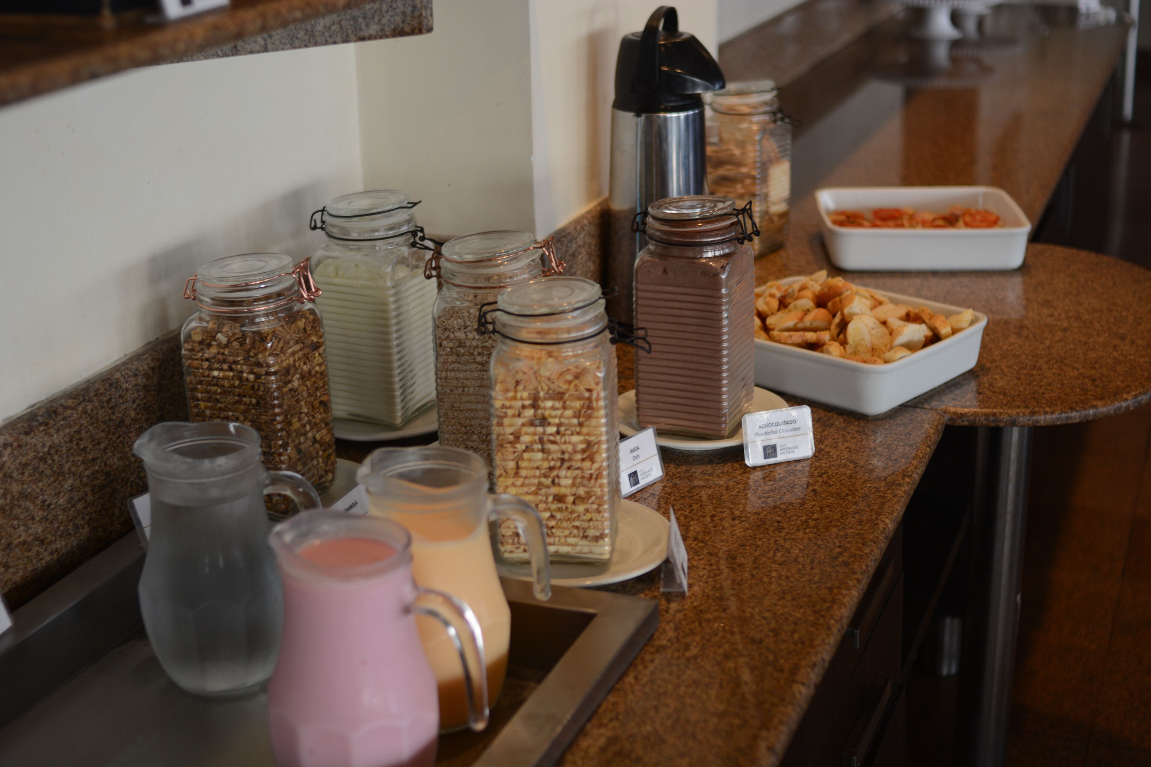 A breakfast bar with various food and drink options, including jars of granola, a coffee maker, and a tray of pastries.