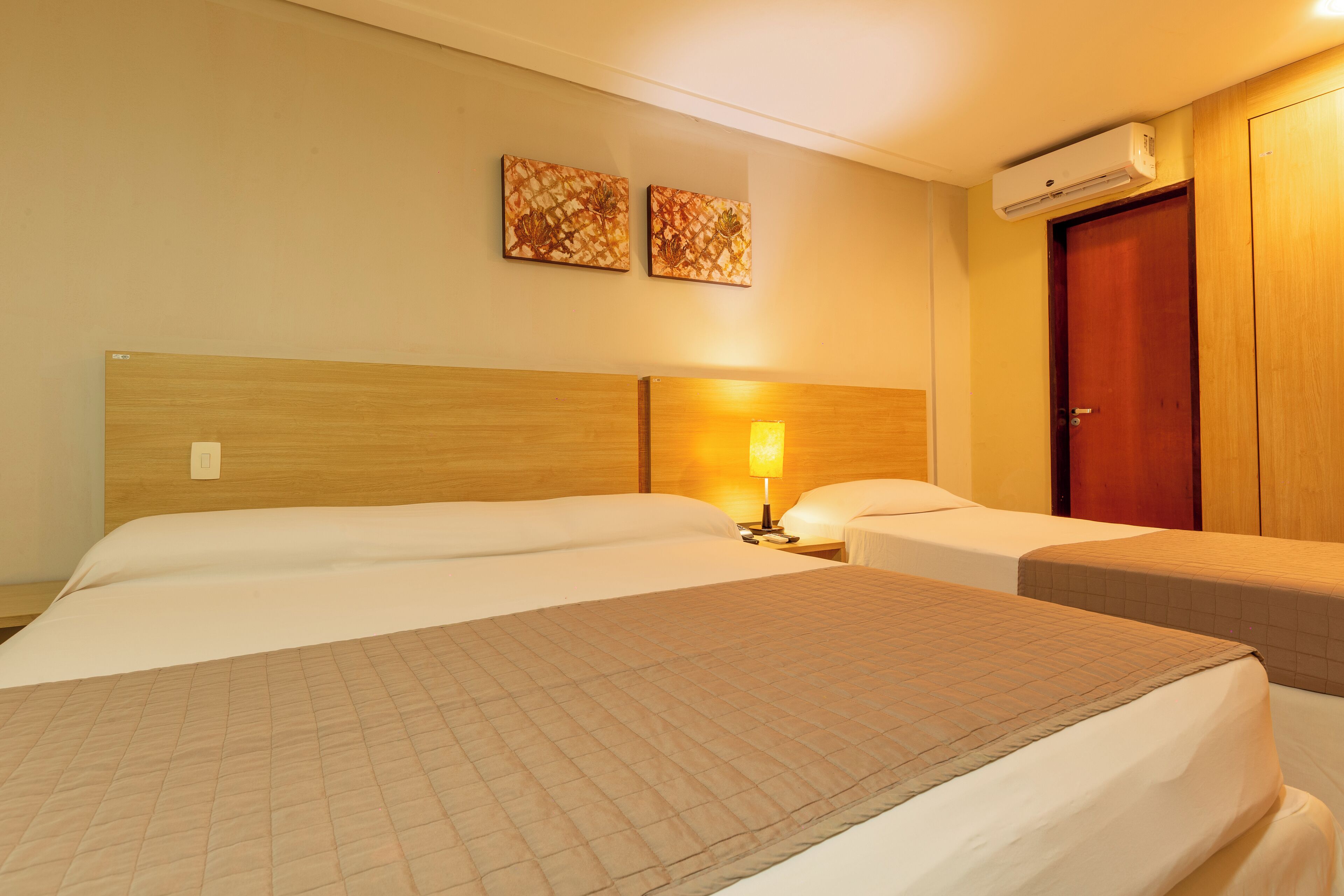 Une chambre d’hôtel avec deux lits, une tête de lit en bois, un climatiseur fixé au mur et une porte.