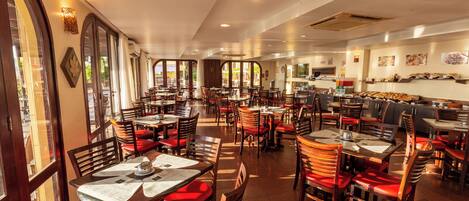 Un restaurant spacieux doté de plusieurs espaces de restauration, de grandes fenêtres et d’une variété de types de sièges, notamment des tables et des banquettes.