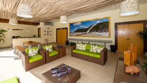 A lobby with wicker sofas, a coffee table, and a large beach mural. - Rede Andrade Bello Mare Comfort (Natal)