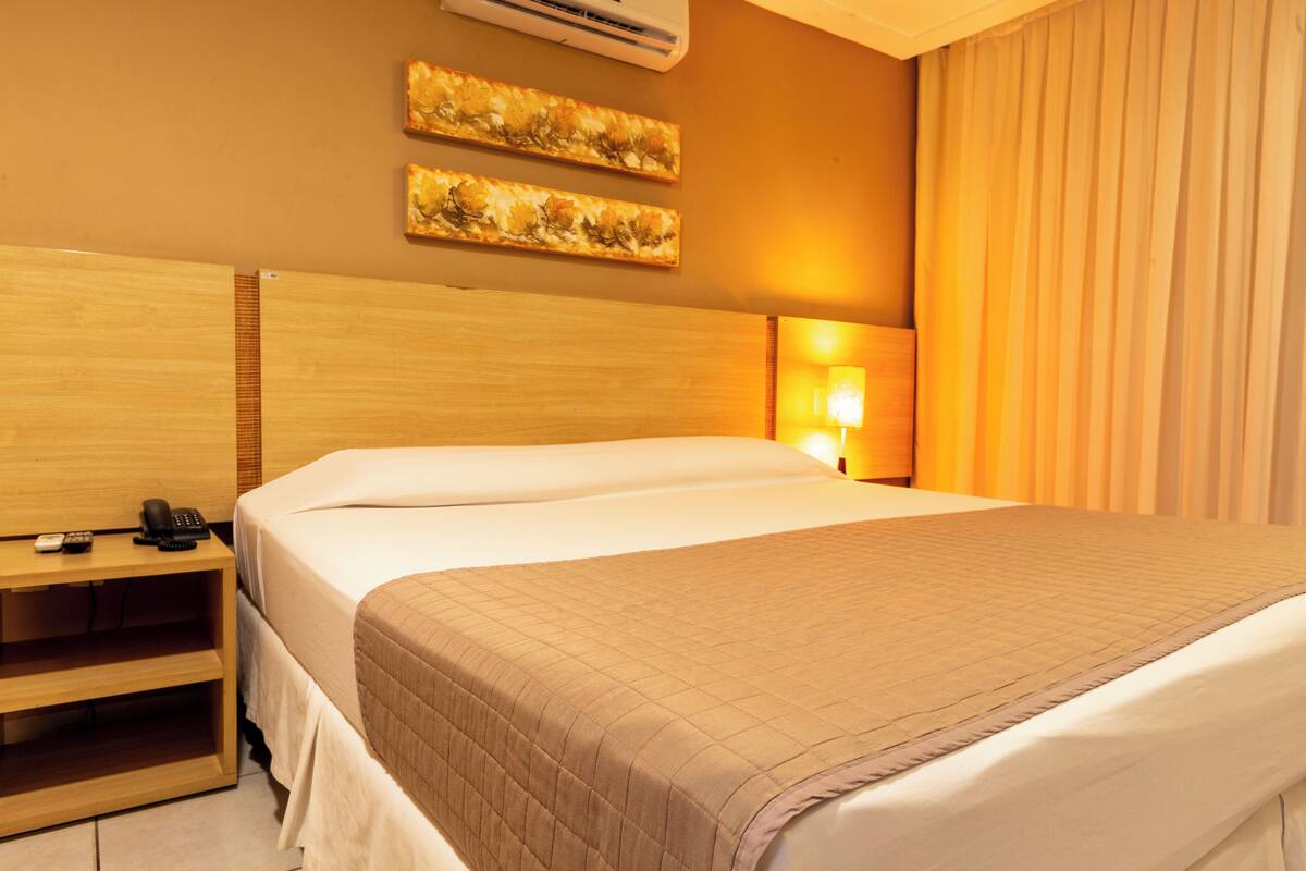 A hotel room with a wooden headboard, a bedside table with a telephone, and a wall-mounted air conditioner.