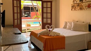 Habitació d'hotel amb llit, taula petita, televisió i vistes a una piscina i palmeres.