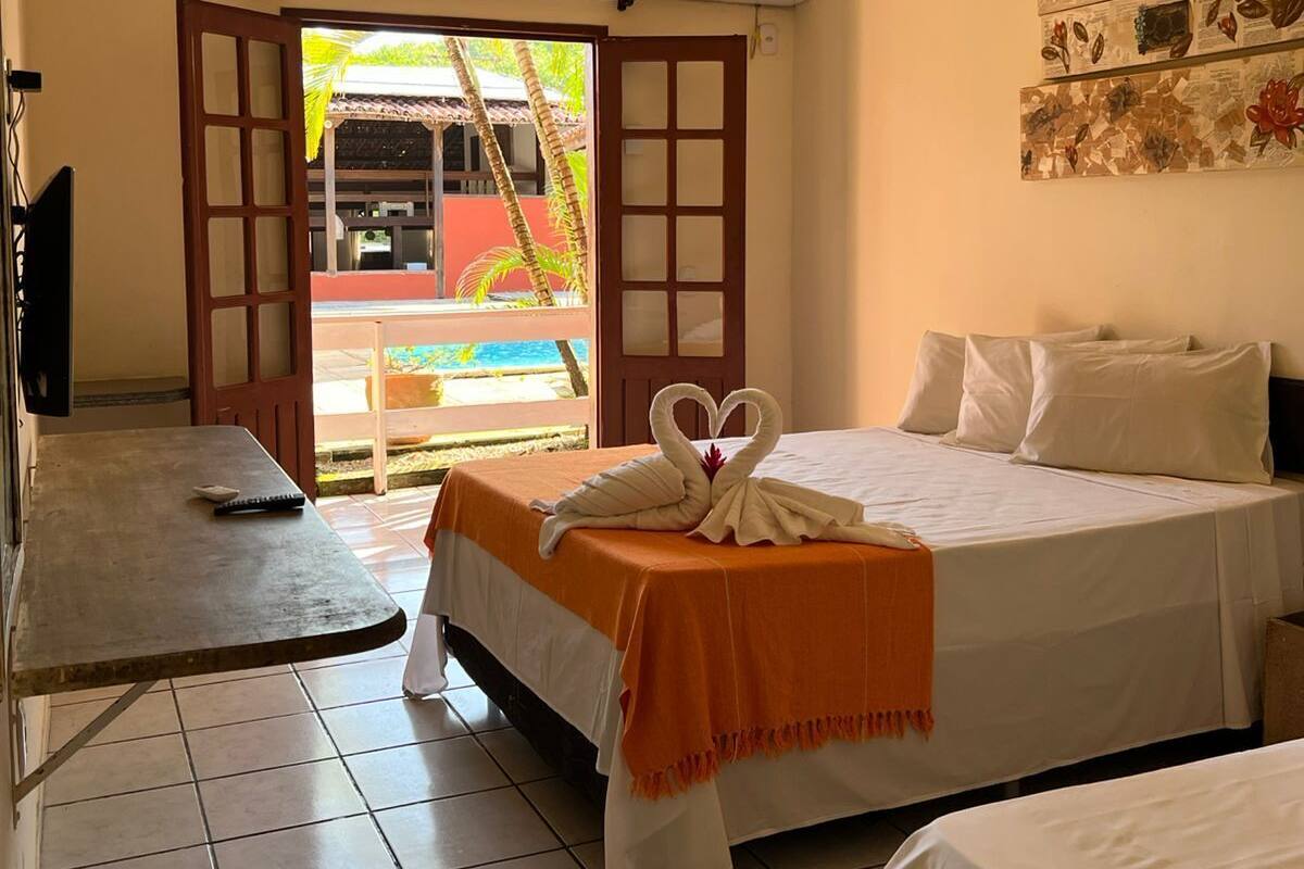 Une chambre d’hôtel avec un lit, une petite table, une télévision et une vue sur une piscine et des palmiers.