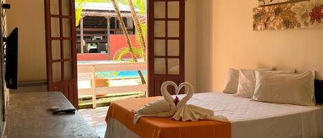 A hotel room with a bed, a small table, a TV, and a view of a pool and palm trees.