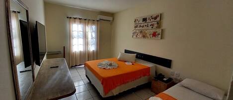A hotel room with two beds, a TV, a desk, and a window with curtains.