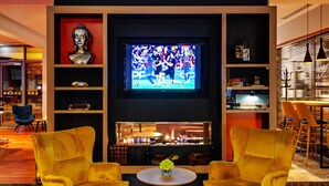 A modern living room with a fireplace, two yellow armchairs, a TV displaying a sports event, and a bookshelf with various items. - Qubus Hotel Bydgoszcz (Bydgoszcz)