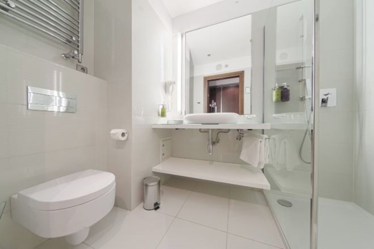 A modern bathroom with a toilet, a sink, a mirror, and a shower area.