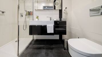 Un baño moderno con cabina de ducha de vidrio, lavamanos blanco, tocador negro, inodoro y un cubo de basura.